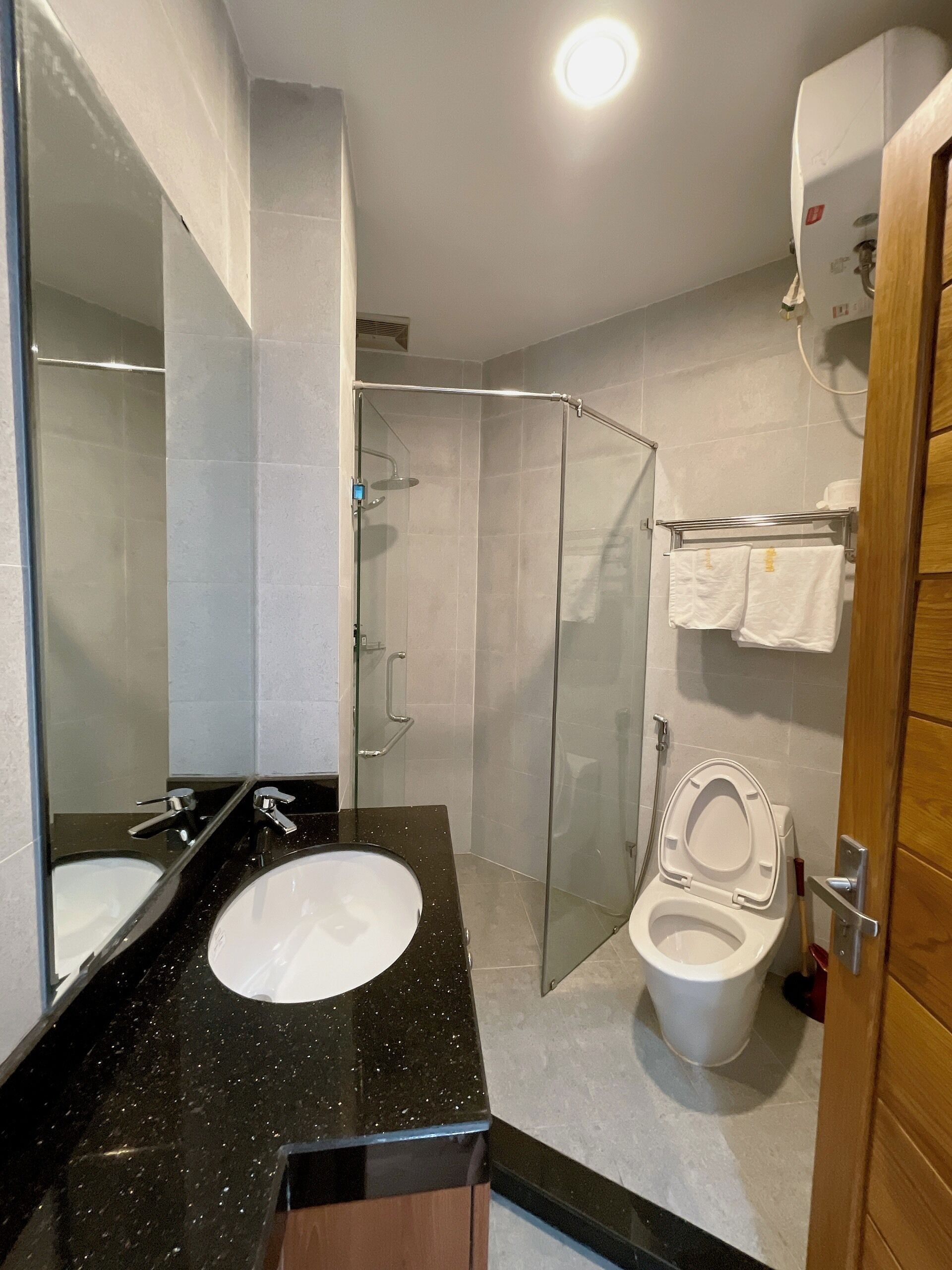 Une salle de bain avec un lavabo à vasque et un plan de toilette noir, des toilettes blanches, une douche en verre et une porte en bois.
