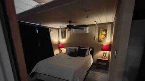 Ein Schlafzimmer mit einem Bett, zwei Nachttischen mit Lampen, einem Deckenventilator und einer Klimaanlage.
