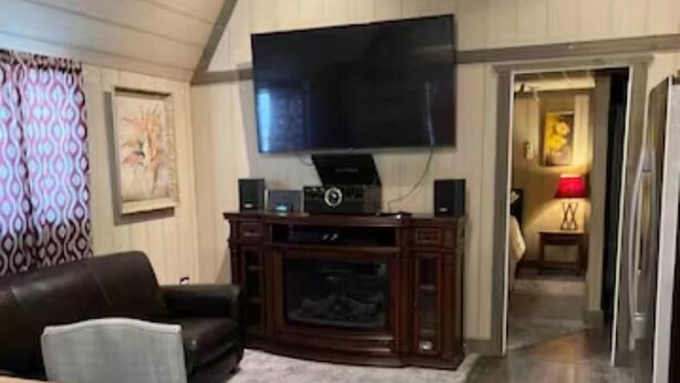 Ein Wohnzimmer mit einem großen Flachbildfernseher, dunklem Holzboden, einem gemusterten Teppich, einem dunkelbraunen Ledersofa und einem hellblauen Sessel.
