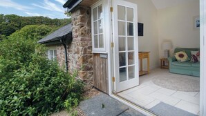 A stone house with a large glass door leading to a living area with a sofa and a lamp.