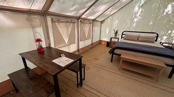 Una habitación con carpa, una mesa de madera, una cama y una pequeña mesa con un farolillo rojo.