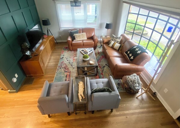 Uma sala de estar com um sofá de couro marrom, duas poltronas cinzentas, uma mesa de centro e um tapete estampado.