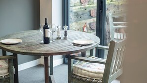 Una mesa redonda de madera con una botella de vino, copas y saleros y pimenteros.