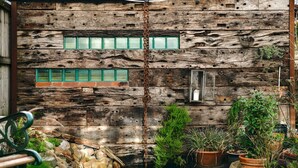 Una construcción rústica de madera con una reja metálica, plantas en macetas y un camino de piedra.