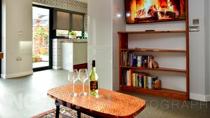 Una sala de estar moderna con chimenea, un televisor montado en la pared y una estantería llena de libros.