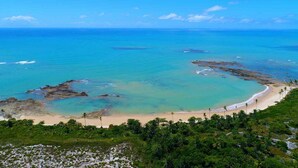 A coastal landscape with a sandy beach, clear turquoise waters, and rocky outcrops. - Ondas Praia Resort - MC (Porto Seguro)
