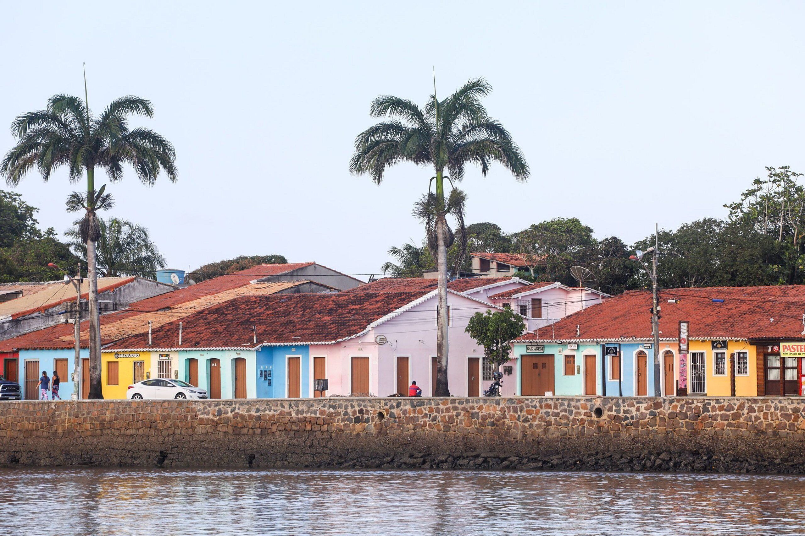 Una calle junto al agua con edificios coloridos, palmeras y un muro de piedra.