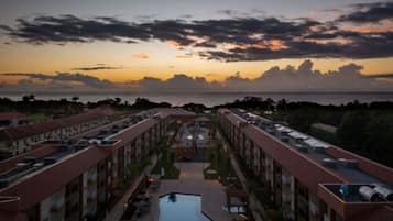 Un hotel con piscina central, varios pisos y vista al mar al atardecer.