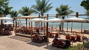 A beachside café with wooden tables and chairs, umbrellas, and palm trees. - Ondas Praia Resort - MC (Porto Seguro)