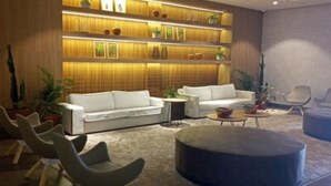 A modern lobby with a white sofa, a round ottoman, and a seating area with chairs. - Ondas Praia Resort - MC (Porto Seguro)