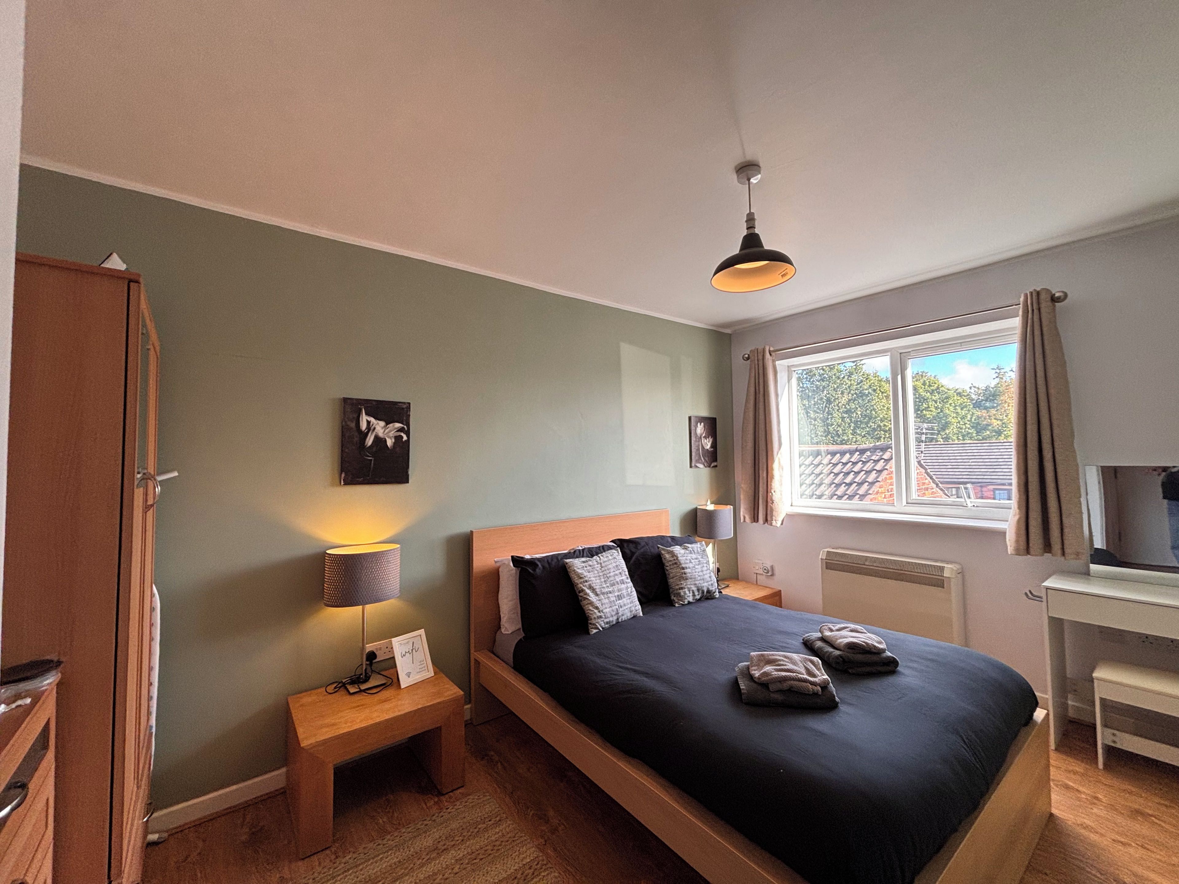 A bedroom with a bed, bedside lamps, a desk, and a window with curtains.