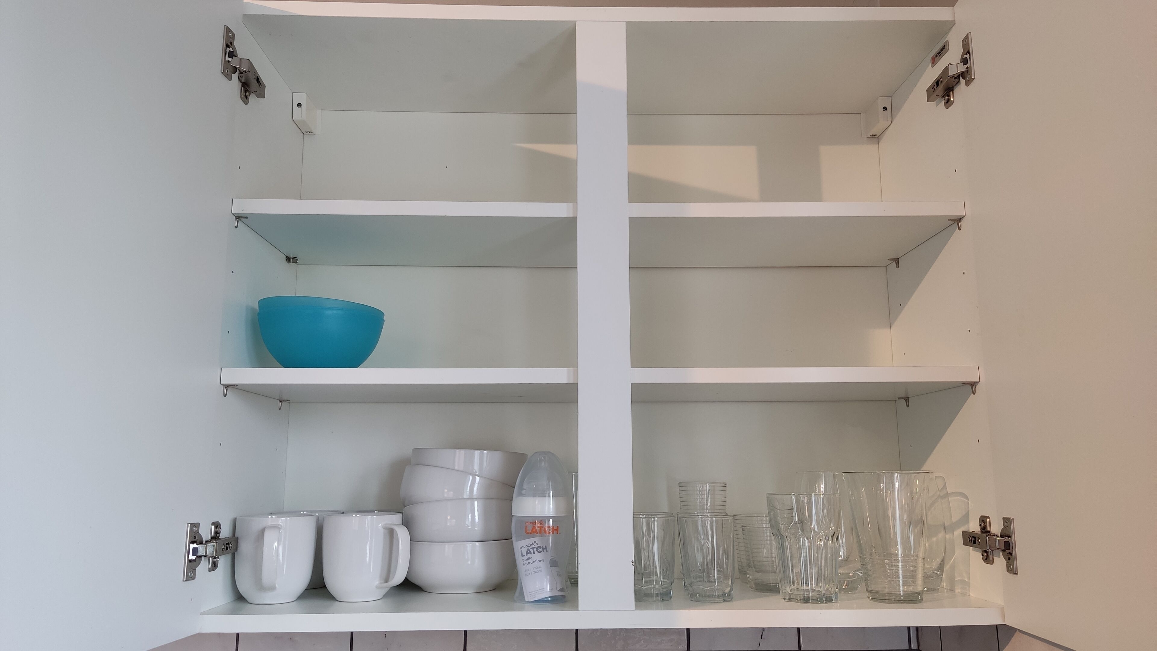 Ein Küchenschrank mit Regalen, der eine blaue Schüssel, weiße Tassen und klare Gläser enthält.