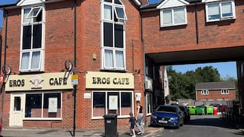 Un edificio de ladrillo de dos pisos con una cafetería llamada 'Eros Cafe' en la planta baja. El cielo está despejado y hay un coche estacionado en primer plano.