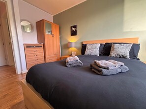 A neatly made bed with folded towels, a wooden wardrobe, a bedside lamp, and a wall-mounted picture. - Stylish 1-Bed Flat | Free Parking · Netflix · In-Unit Laundry (Wigan,)