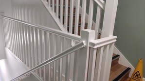 Una escalera blanca con barandilla de metal y un cono amarillo de precaución que indica superficie resbaladiza.