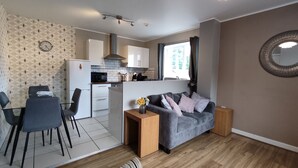 Un espacio habitable compacto con kitchenette, comedor y zona de estar con sofá y una pequeña mesa.