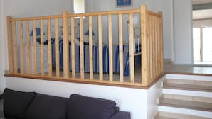 Une pièce avec un escalier en bois, un lit avec une literie bleue, un canapé de couleur sombre et un tableau encadré au mur.