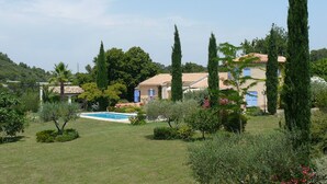 Une villa avec piscine, entourée d’une végétation luxuriante et de grands cyprès.