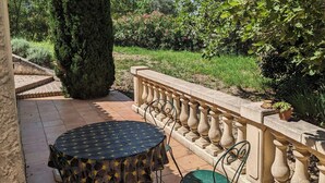 Une terrasse avec une table ronde et deux chaises, un grand cyprès et une balustrade en pierre.