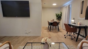 Ein modernes Wohnzimmer mit Flachbildfernseher, Couchtisch mit Vase und Essbereich mit Stühlen und Tisch.