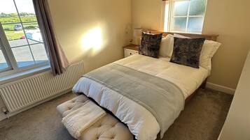 Un dormitorio con una cama grande, un banco, una ventana con cortinas, un radiador y una lámpara en el techo.