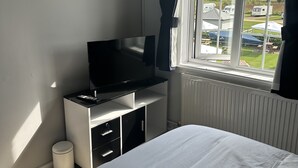 A bedroom with a bed, a TV on a stand, a radiator, and a window with curtains.