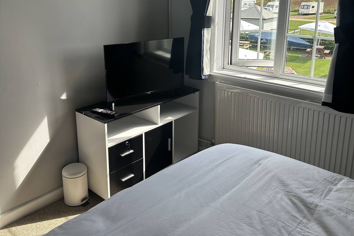 A bedroom with a bed, a TV on a stand, a radiator, and a window with curtains.