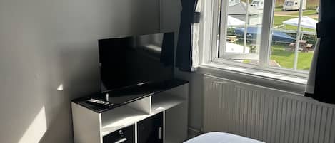 A bedroom with a bed, a TV on a stand, a radiator, and a window with curtains.