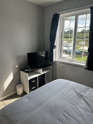 A bedroom with a bed, a TV on a stand, a radiator, and a window with curtains.