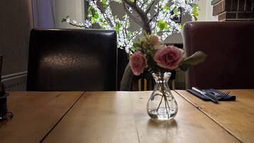 A dining table with a vase of pink flowers and a candle.