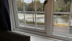 Une fenêtre donnant sur une rivière et des arbres, une lampe posée sur le rebord de la fenêtre et un rideau qui recouvre partiellement la fenêtre.
