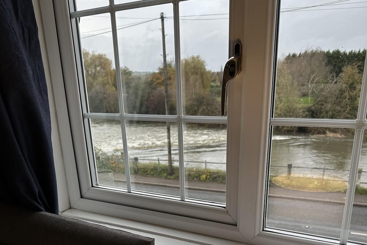 A window with a view of a river and trees, a lamp on the windowsill, and a curtain partially covering the window.