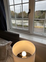 A window with a view of a river and trees, a lamp on the windowsill, and a curtain partially covering the window.