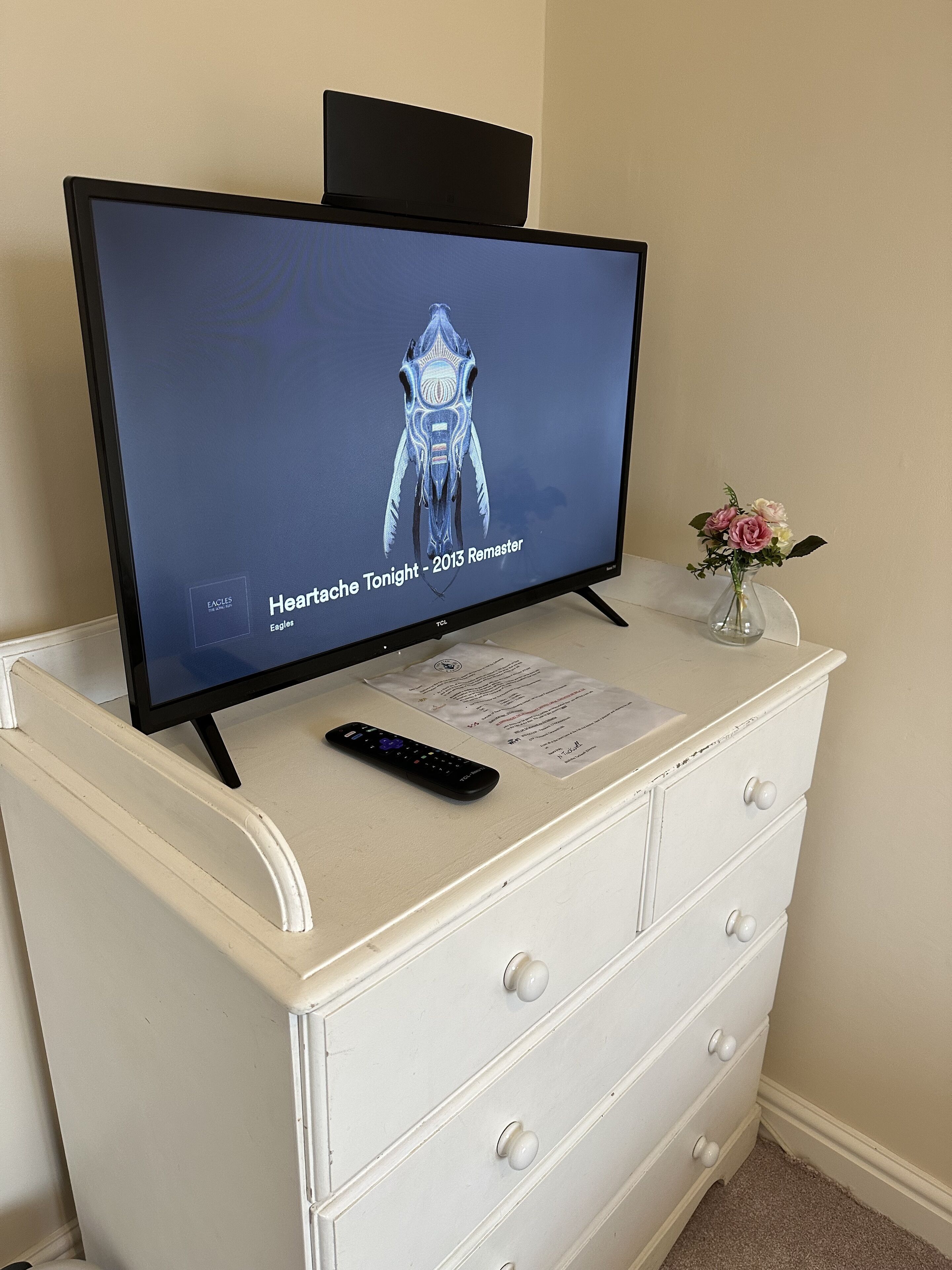 Un televisor sobre un tocador blanco, con control remoto y una tarjeta de menú.