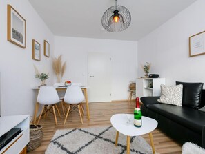 A modern living room with a white sofa, a dining table with chairs, a small white coffee table with a bottle, and a unique pendant light. - Apartment Möwe by Interhome (Zinnowitz)