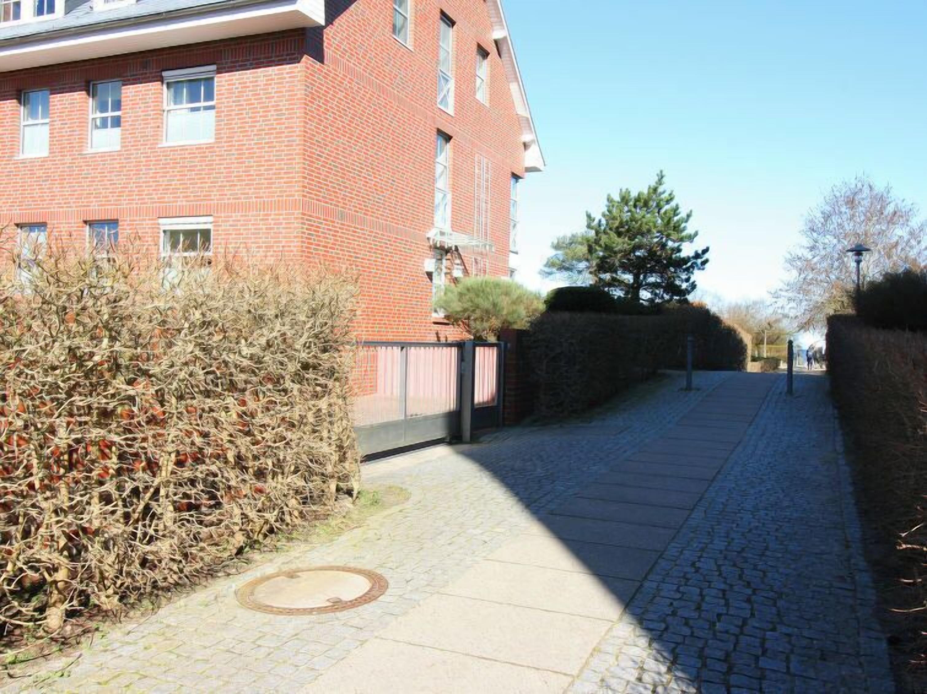 Un bâtiment en briques doté de nombreuses fenêtres, un chemin pavé et une haie.