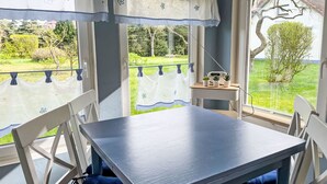 Ein Zimmer mit Tisch und Stühlen, einem Fenster mit Blick auf Grünflächen und einem kleinen Tisch mit Blumentöpfen.