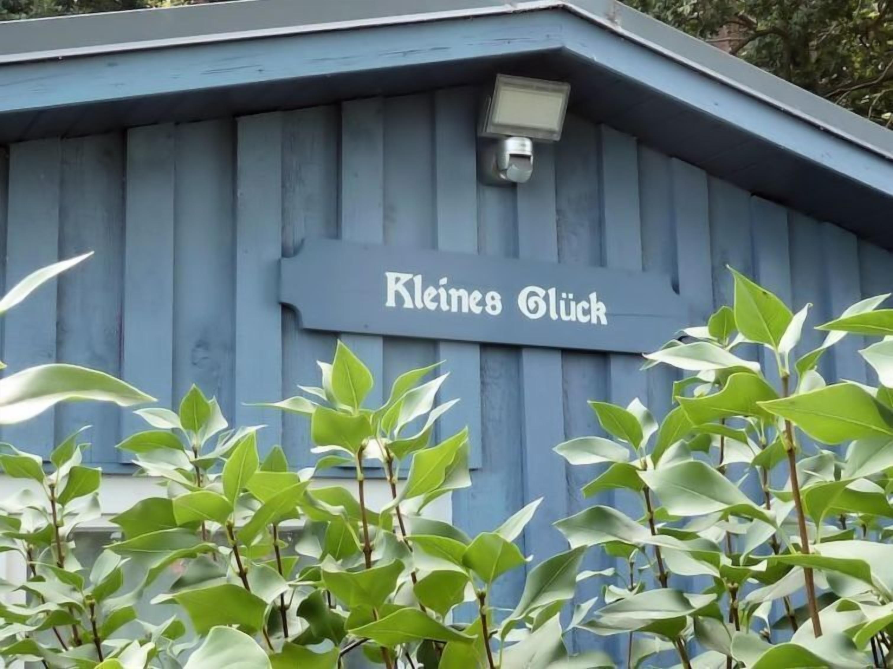 A building with a sign that reads "Kleines Glück" and a security camera mounted on the roof.