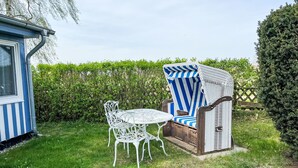 Eine Terrasse mit Tisch und Stühlen, ein gestreifter Stuhl und ein kleines Gartenhaus.
