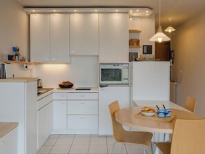 Una cocina moderna con muebles blancos, un microondas y un comedor con mesa y sillas de madera.