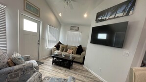 A living room with a beige sofa, patterned armchairs, a coffee table, and a flat-screen TV mounted on the wall. - Historical Cottage in Downtown Lake Worth Beach, fully renovated and modernized (Lake Worth)