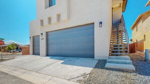 A modern two-story building with a large garage door, a staircase leading to the upper level, and a stop sign visible in the background. - New Studio, Balcony w/views, Nexflix, Pool
 (Albuquerque)