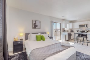 A modern hotel room with a large bed, a small bedside table with a lamp, a view of the balcony, and a kitchenette area. - New Studio, Balcony w/views, Nexflix, Pool
 (Albuquerque)