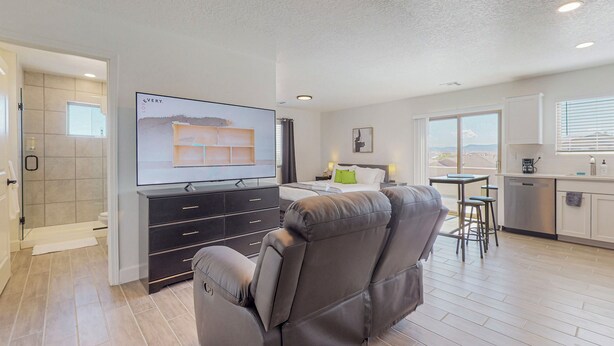 A modern living room with a reclining chair, a flat-screen TV, a bed, a kitchen area, and a view of the outdoors. - New Studio, Balcony w/views, Nexflix, Pool
 (Albuquerque)