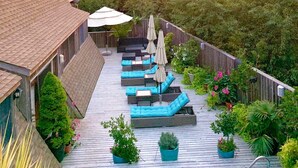 A deck with outdoor seating and a pool, surrounded by lush greenery and a sunset view. - Immaculate Luxury Fire Island Pines Home, Gourmet Kitchen, Pool, Hot Tub Private (Fire Island Pines)