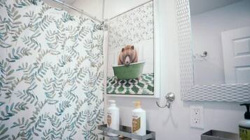 A bathroom with a leaf-patterned shower curtain, a framed picture of a bear in a bowl, and a shelf with toiletries.