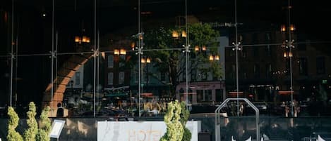 An outdoor seating area with potted plants, a white sign reading "HOTEL", and a view of the cityscape in the background.
