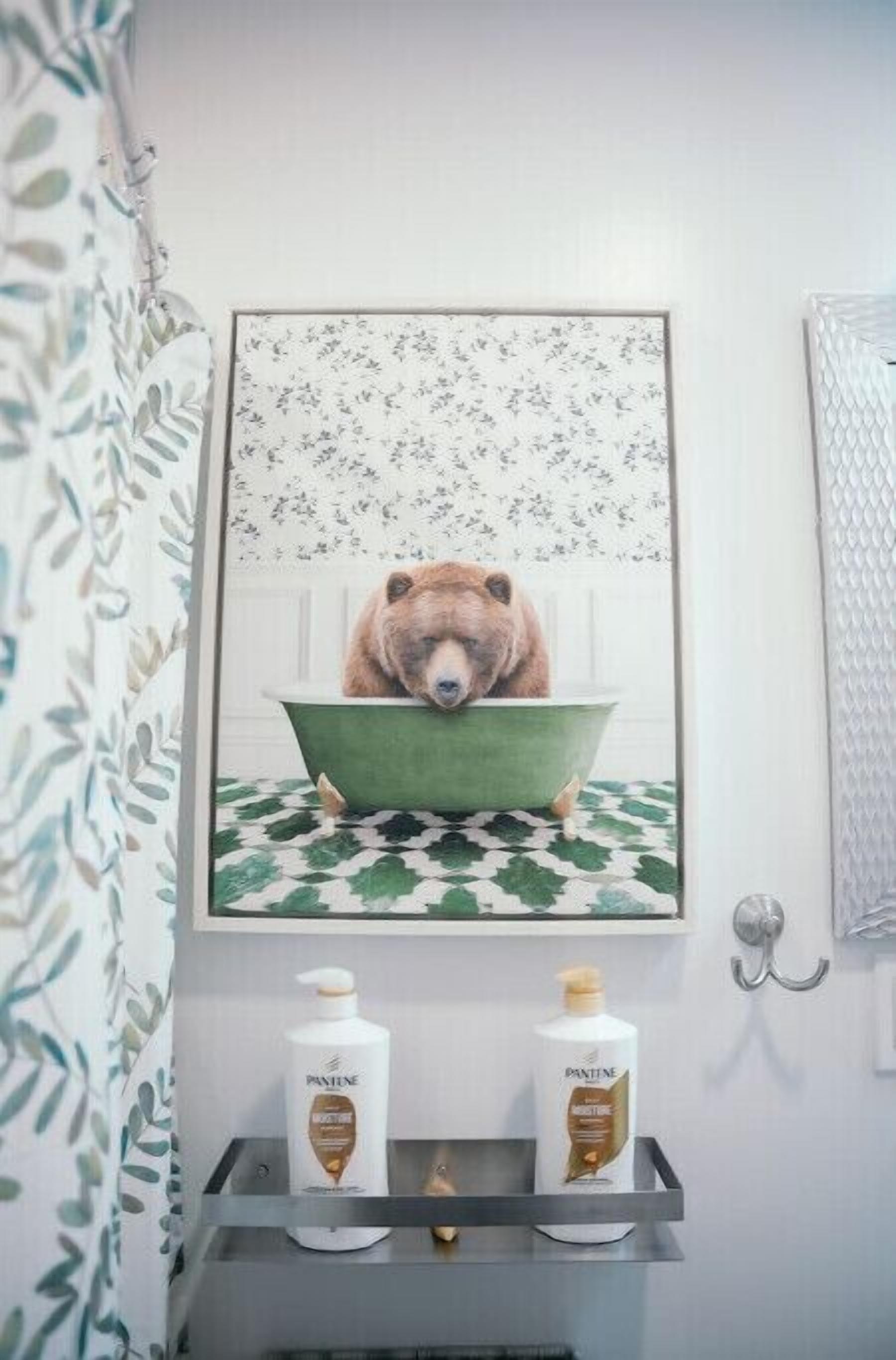 Un baño con una obra de arte temática de osos sobre un lavamanos, dos botellas de champú Pantene y una cortina de ducha estampada.