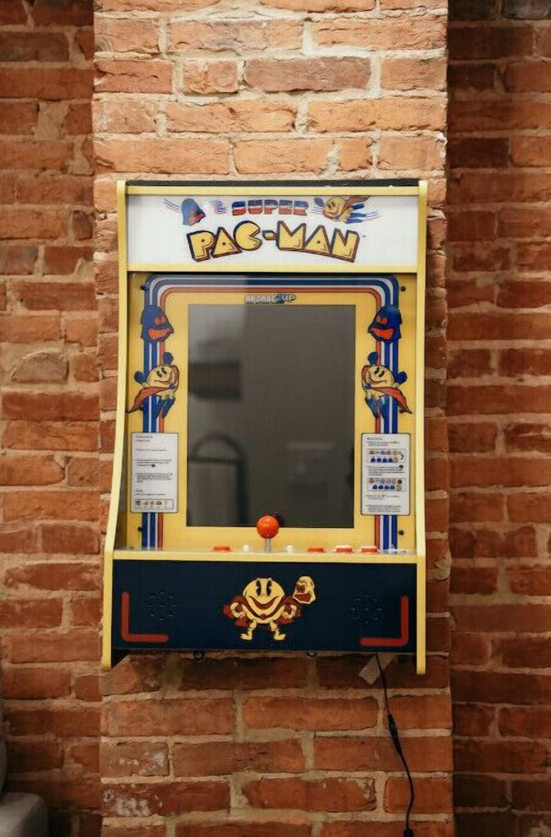 Una máquina de videojuegos Pac-Man fijada en una pared de ladrillos.