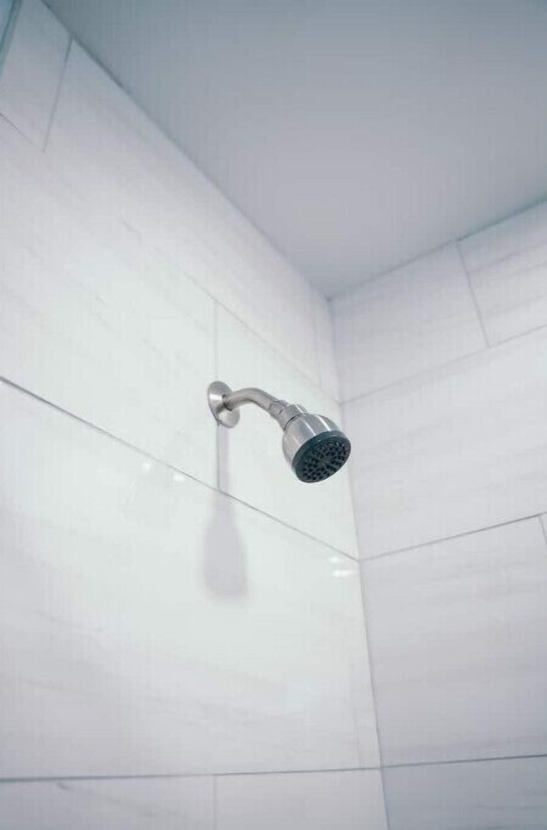Un pommeau de douche fixé sur un mur carrelé de blanc dans une salle de bain.
